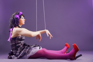 Fashion model stylized as marionette doll sitting on violet studio background